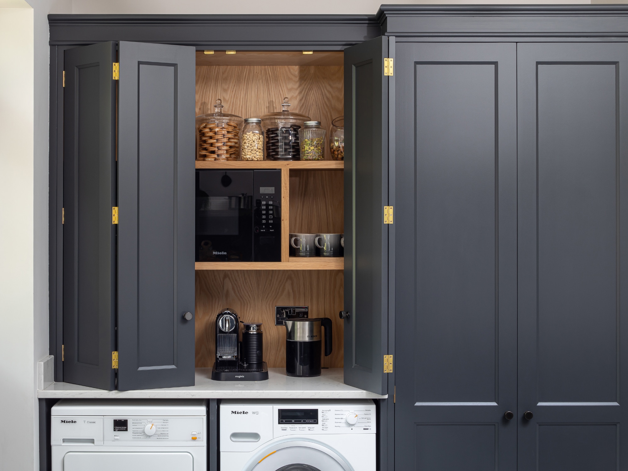 Black painted cabinetry with oak shelving and coffee machine, washing machine and tumble dryer.